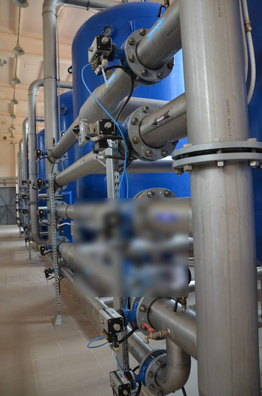 Stainless steel valve manifold gallery between pressure multimedia filter vessels showing automated actuated butterfly valves and pressure gauges